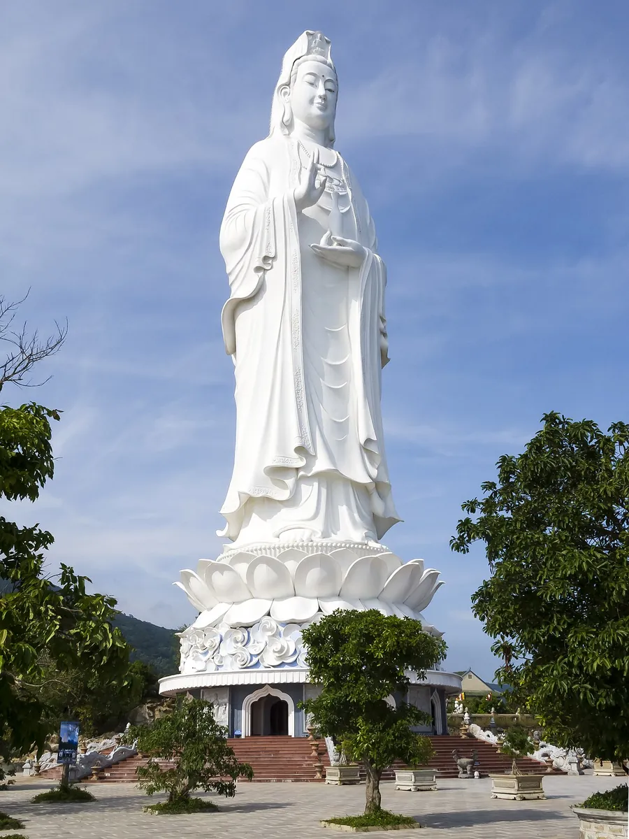 The 67 m white Lady Buddha statue on a lotus base, seen from below with trees on both sides