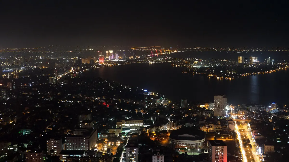 Night view from the tower over lit streets and a dark lake, with the city lights stretching to the horizon
