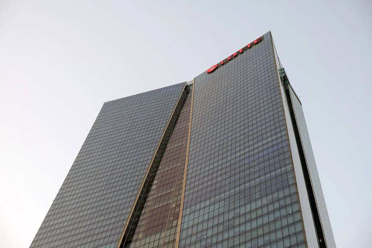 A dark glass skyscraper with a sloping, folded face, seen from below against a pale sky
