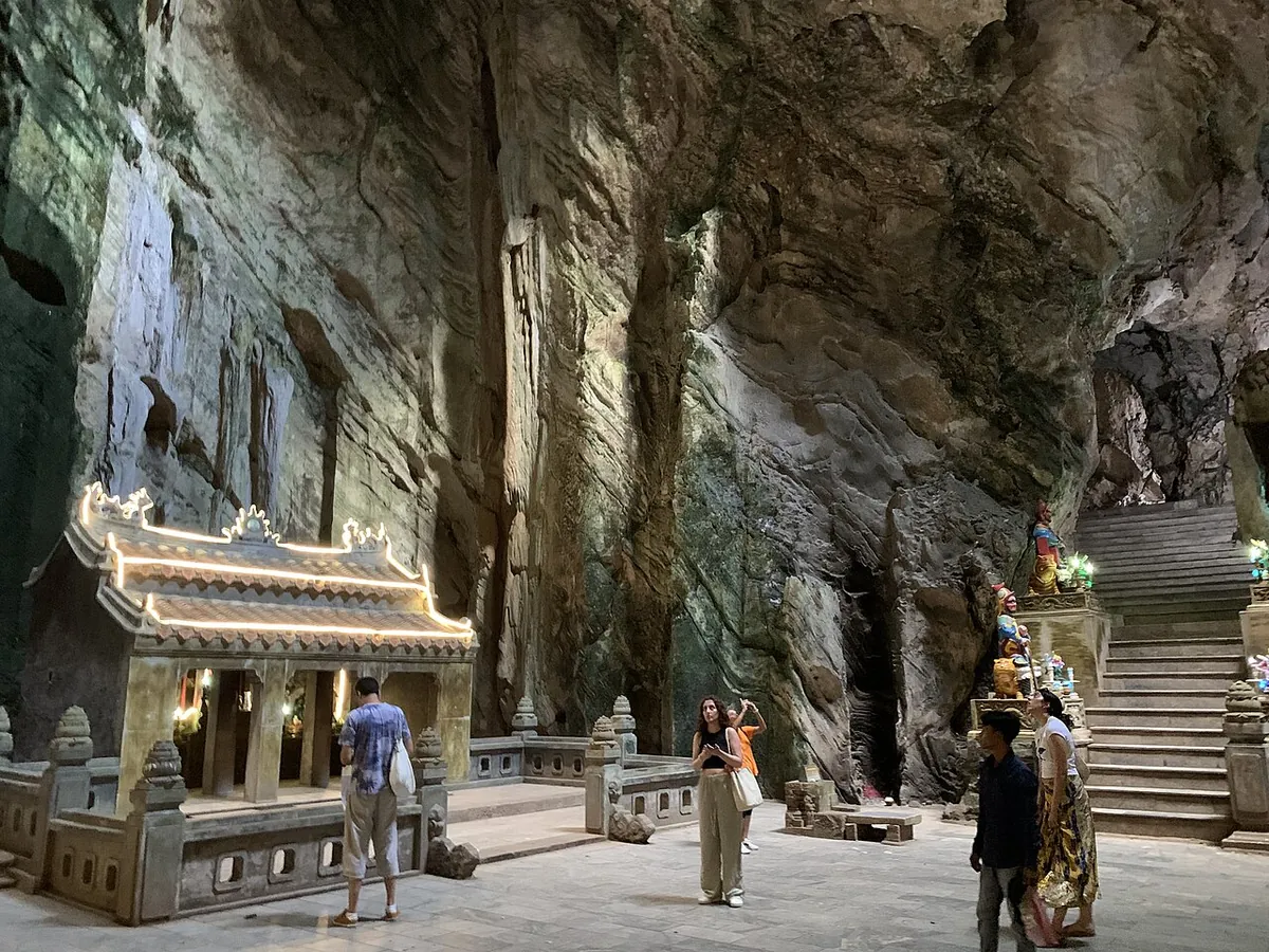 A carved stone gateway inside Huyen Khong cave, with visitors on the paved floor and a stairway cut into the rock