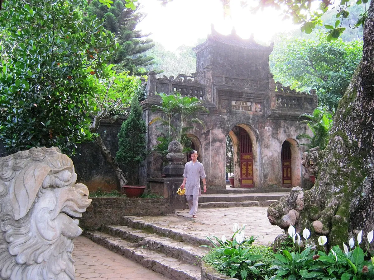 The ornate stone gate of Tam Thai Pagoda with a lion statue in the foreground and trees around the steps