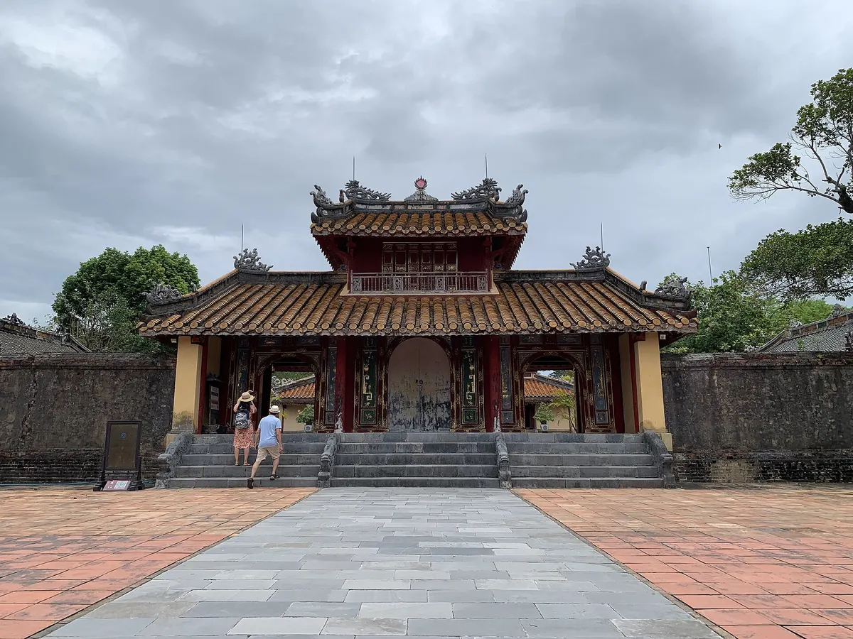 Hien Duc Gate, a wooden gate with three openings and a tiled upper pavilion, at the end of a paved path between walls