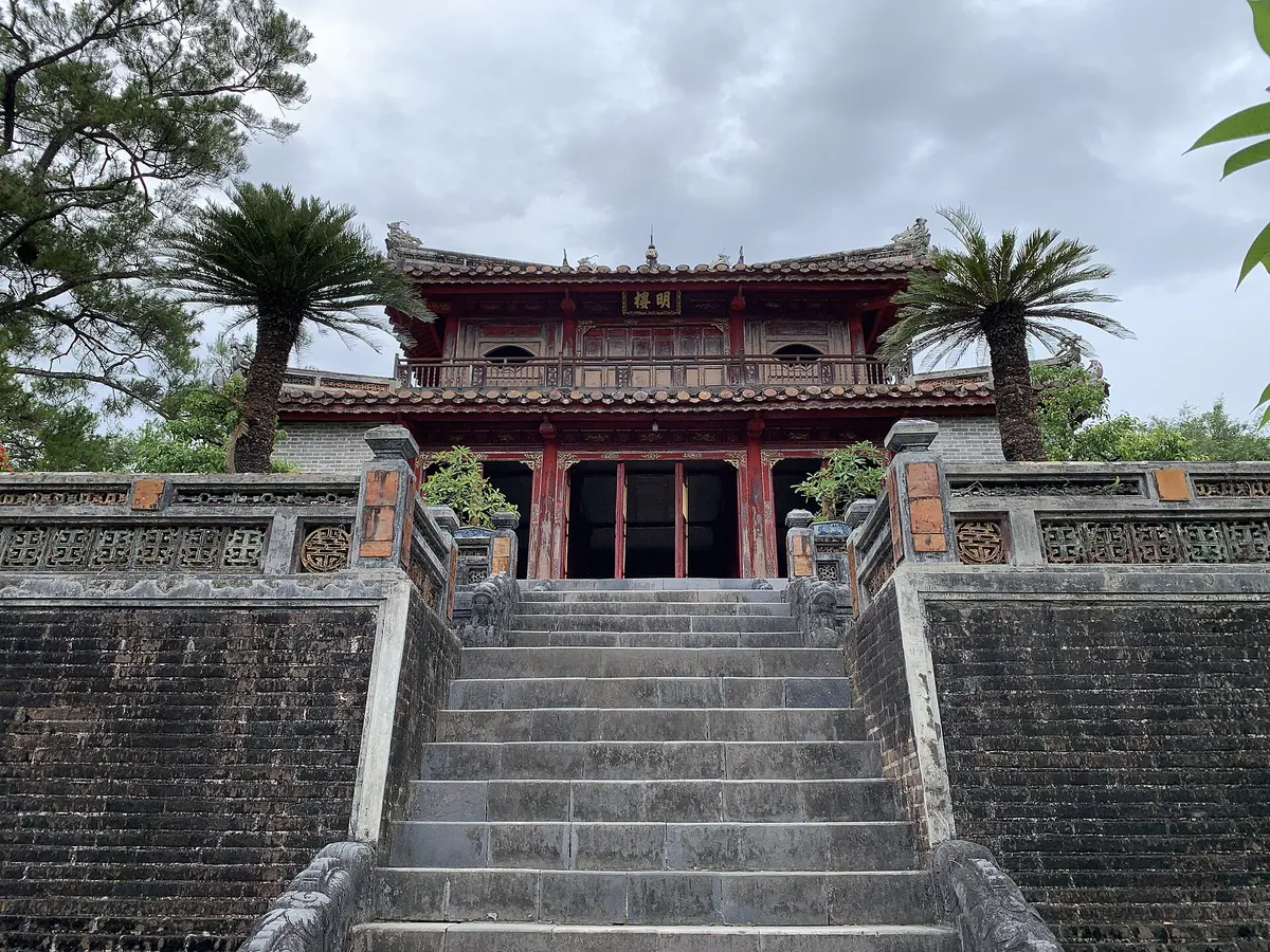 Minh Lau, a two-storey red and gold pavilion at the top of a steep flight of stone stairs, flanked by palms