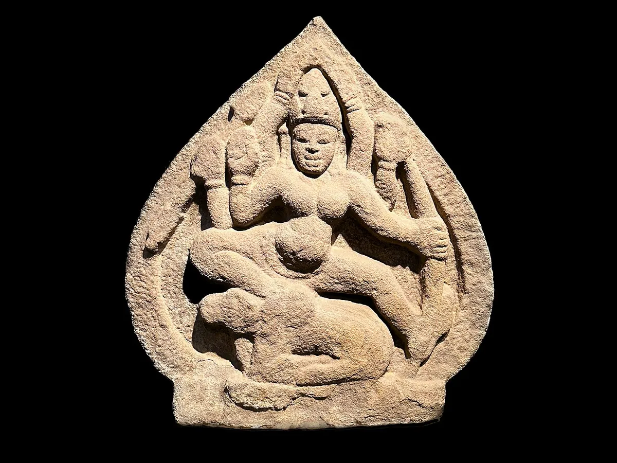 A sandstone relief of the goddess Durga standing on a buffalo, from a Cham temple, displayed against a black background