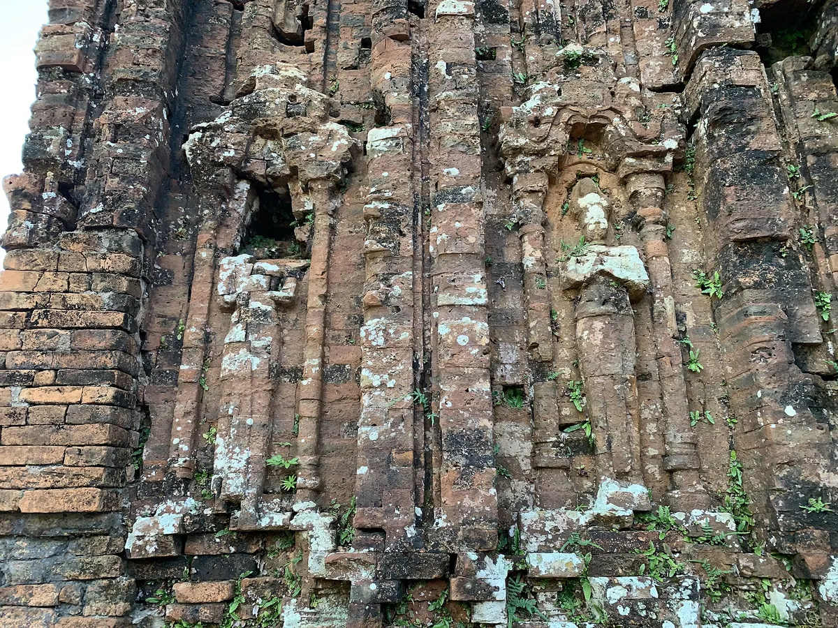 Close view of a brick tower wall at My Son, carved with pilasters and a weathered figure in a niche