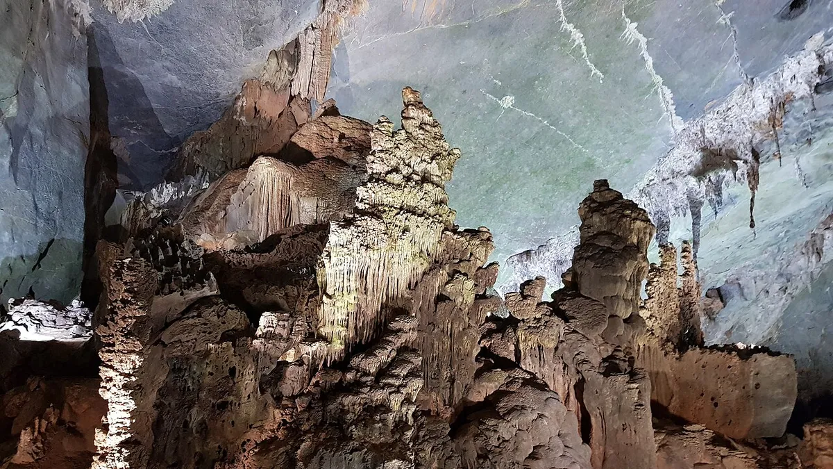 Tall stalagmites and flowstone lit in white and gold inside Phong Nha Cave