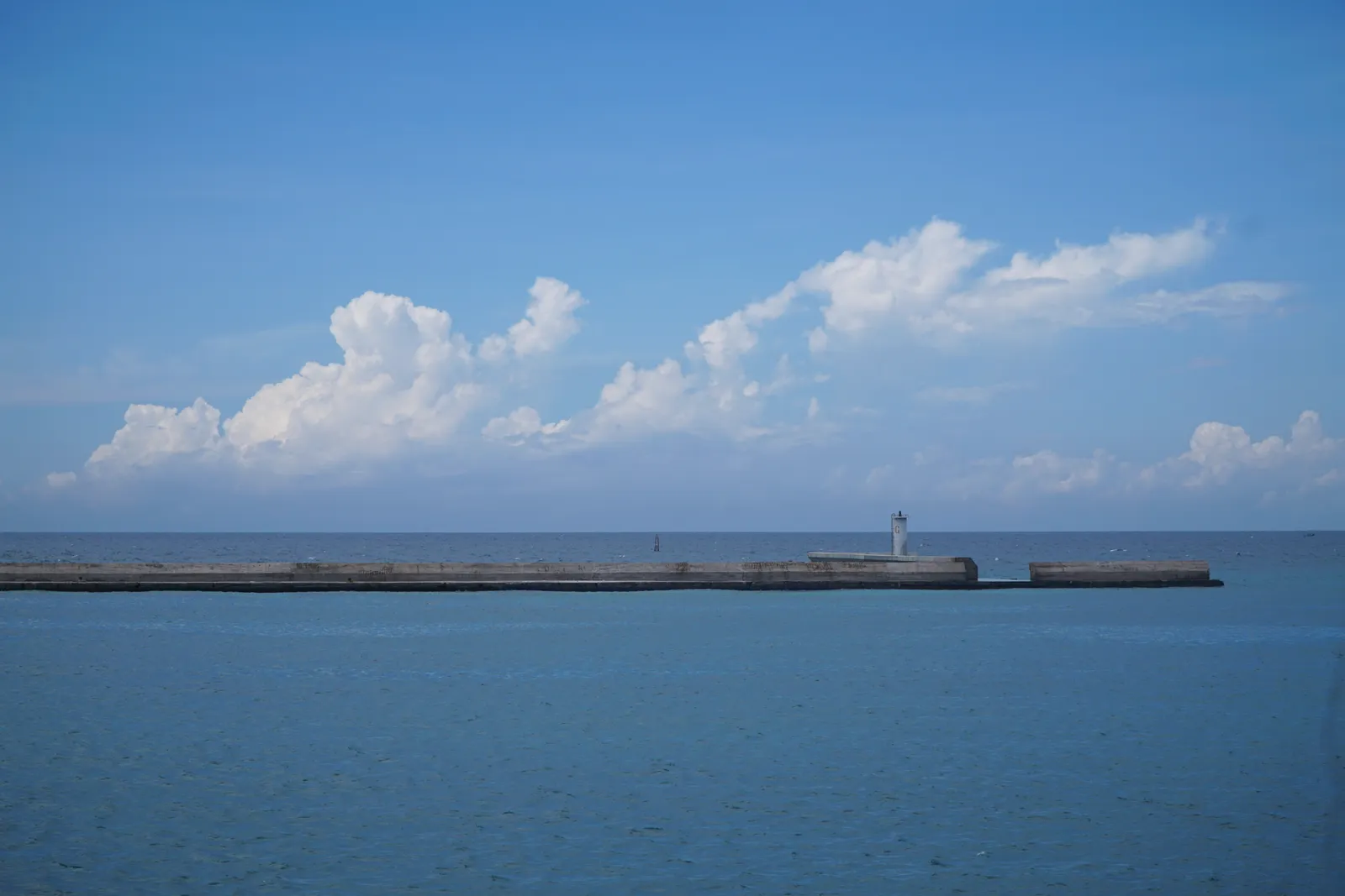 A long breakwater with a harbour light across calm blue water at Phu Quy, white clouds above