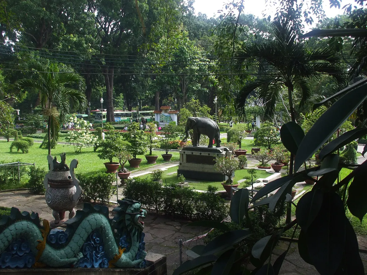 Lawns, potted plants and an elephant statue under tall palms, with a dragon carving in the foreground