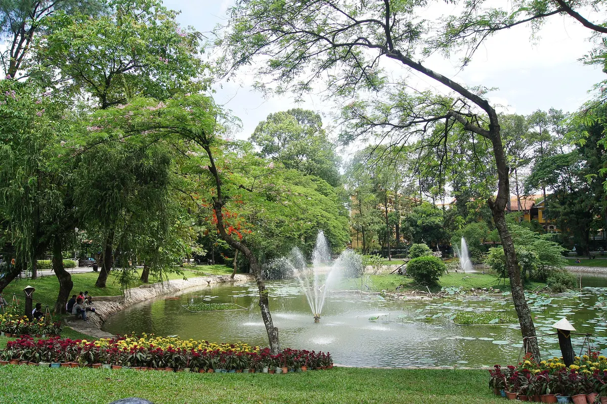 A pond with fountains, flower beds and trees inside the gardens
