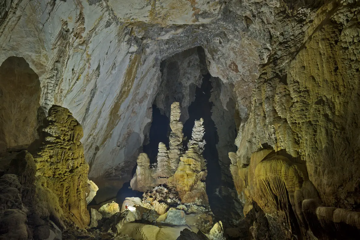 Giant stalagmites rising in the main passage of Son Doong, a caver's lamp tiny at their foot