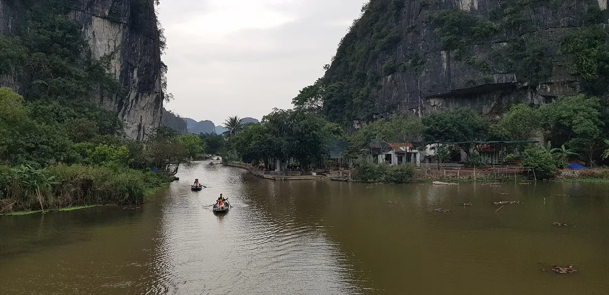 Small boats on the river at Tam Coc, with a sheer limestone cliff rising on the left bank