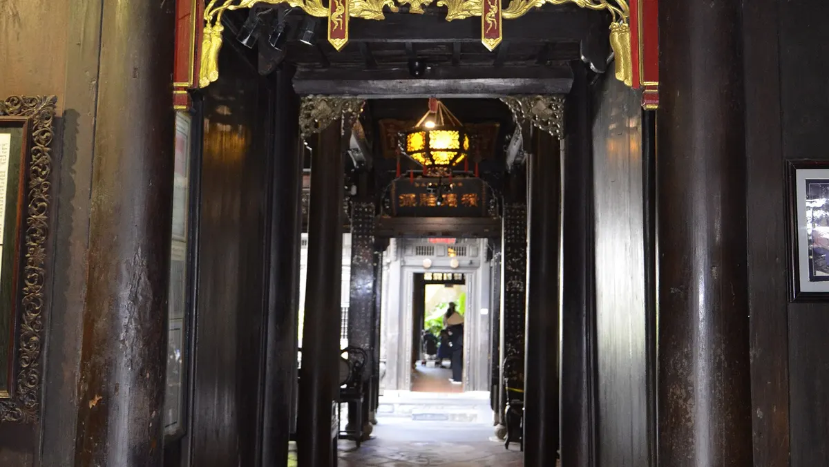A corridor running back through Tan Ky Old House under a gilded name board, with dark wooden pillars and a bright doorway at the far end