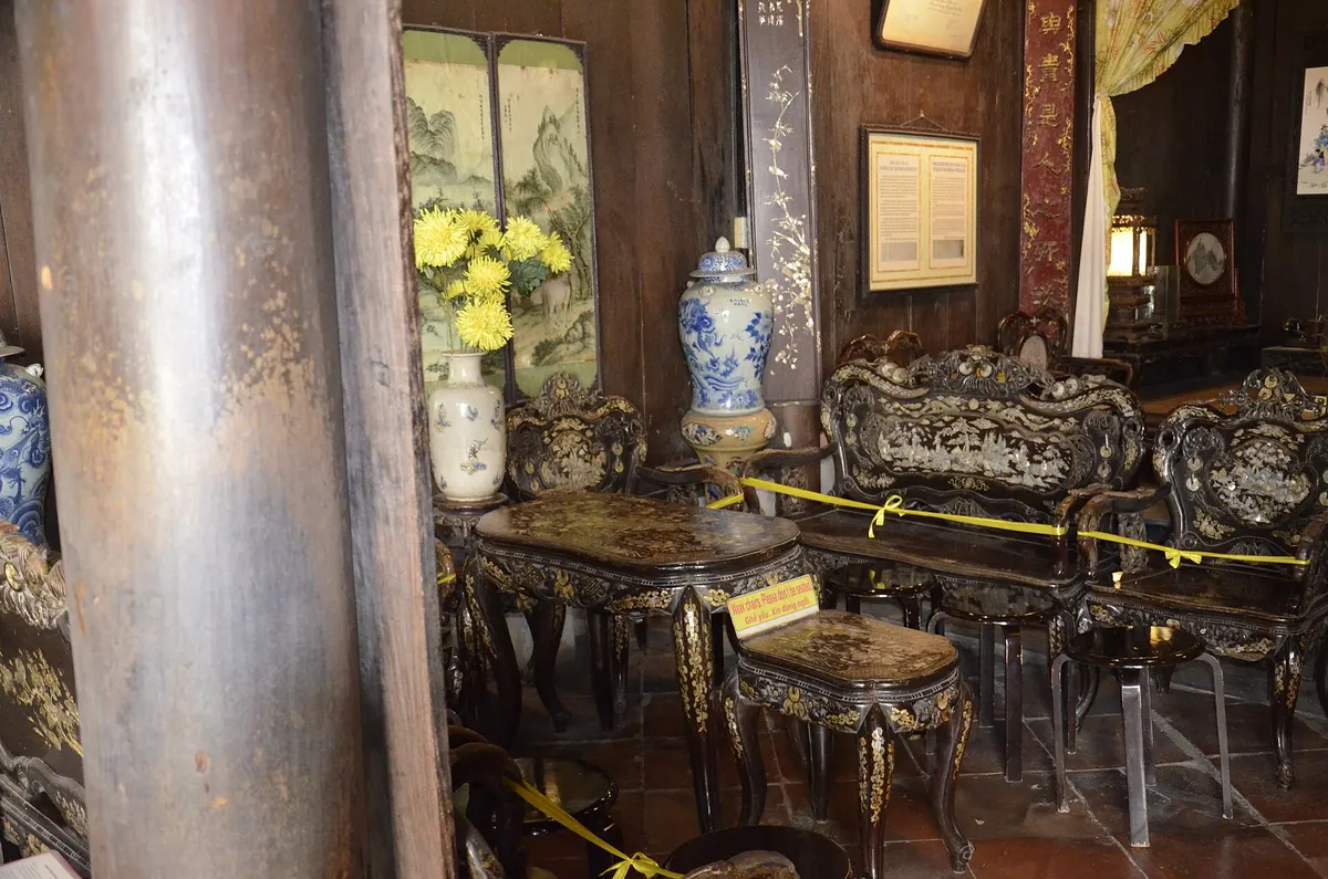A room inside Tan Ky Old House with dark carved chairs and tables inlaid with mother-of-pearl, blue-and-white vases and a wooden column