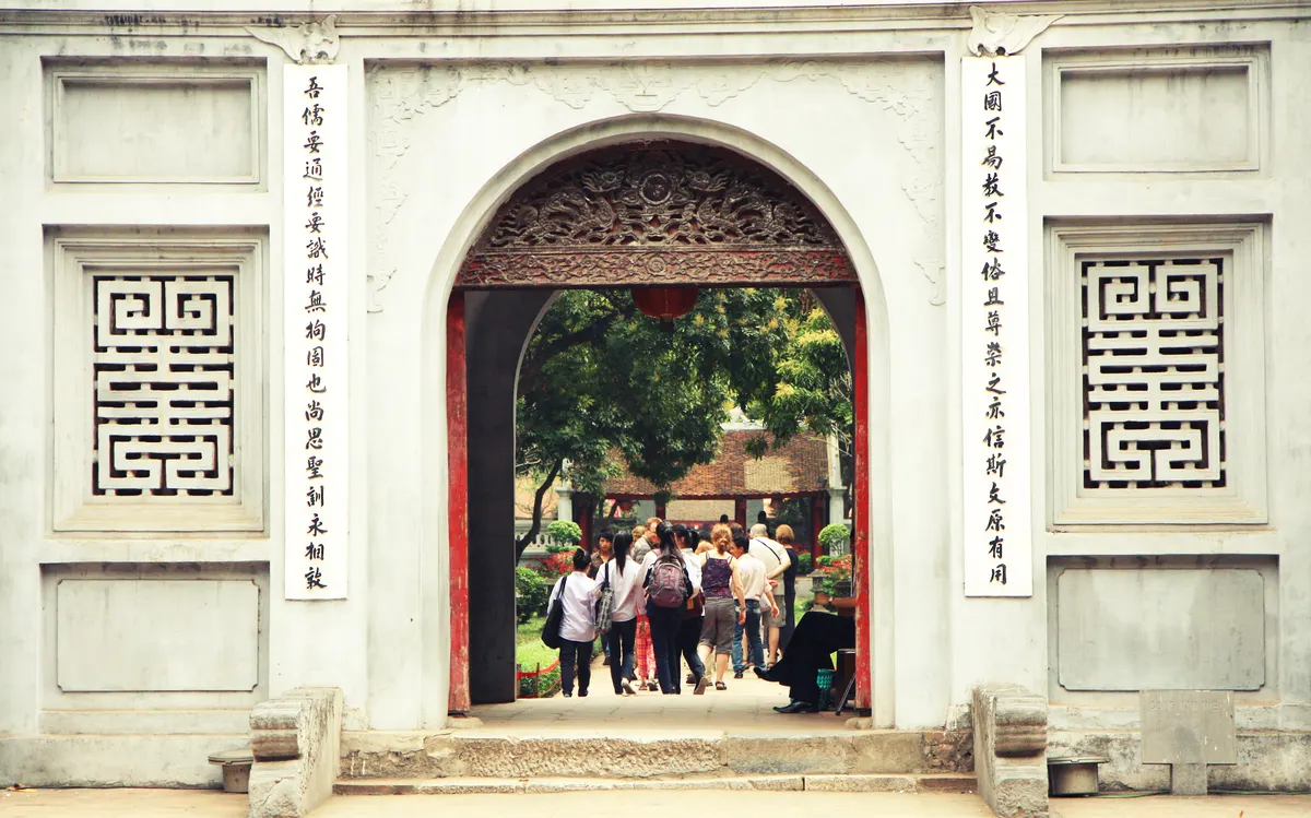 The white arched gate of the Temple of Literature with carved panels and Chinese characters, visitors passing through