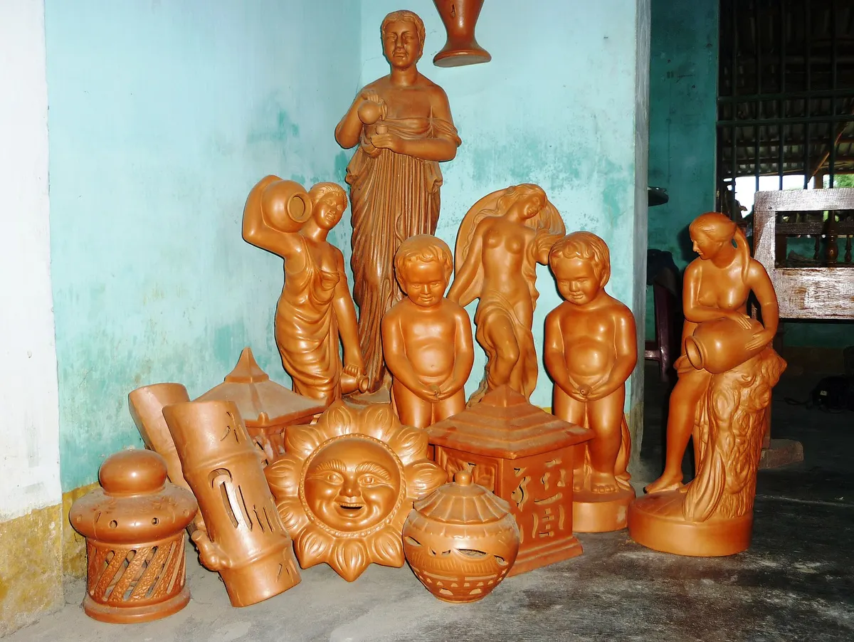 Glazed orange terracotta figures, lanterns and a sun-faced plaque lined up against a pale green wall