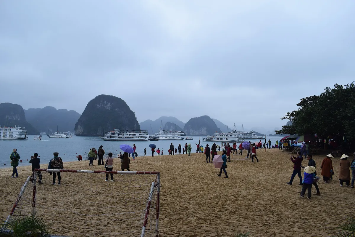 Visitors on a wide sand beach on Ti Top Island, with tour boats and limestone islands under a grey sky
