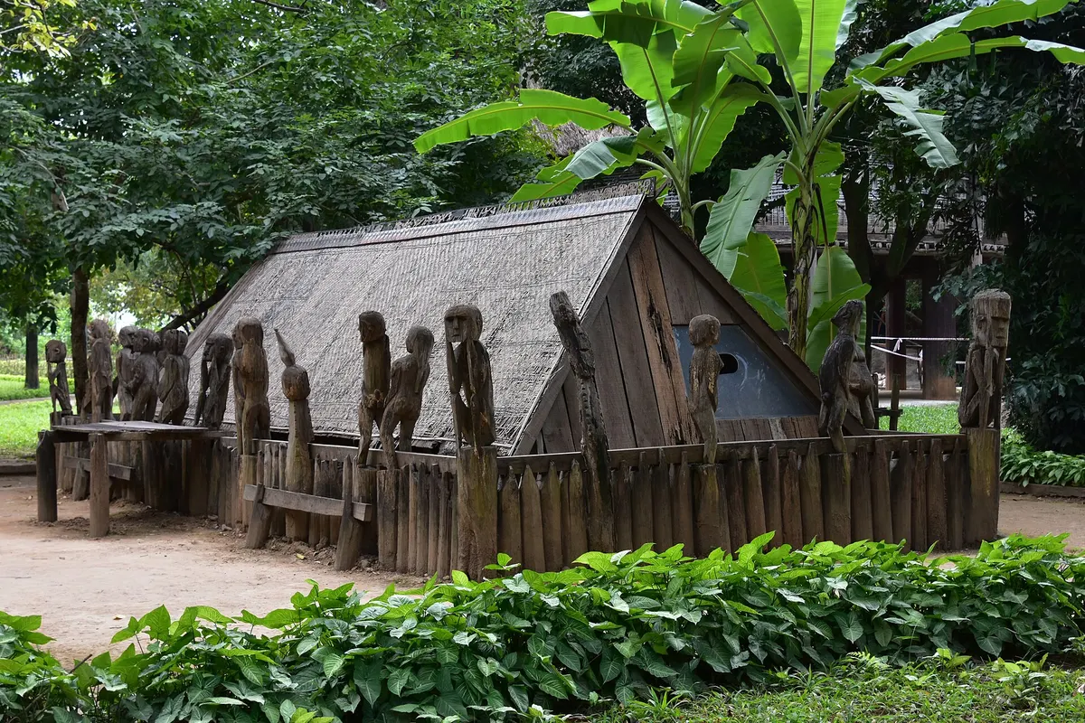 A thatched Giarai tomb house surrounded by a fence of carved wooden figures
