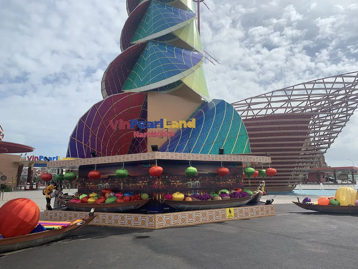 A tall spiral sculpture in bright colors above a stand of hanging lanterns at the park entrance, with a ship-shaped steel frame behind it