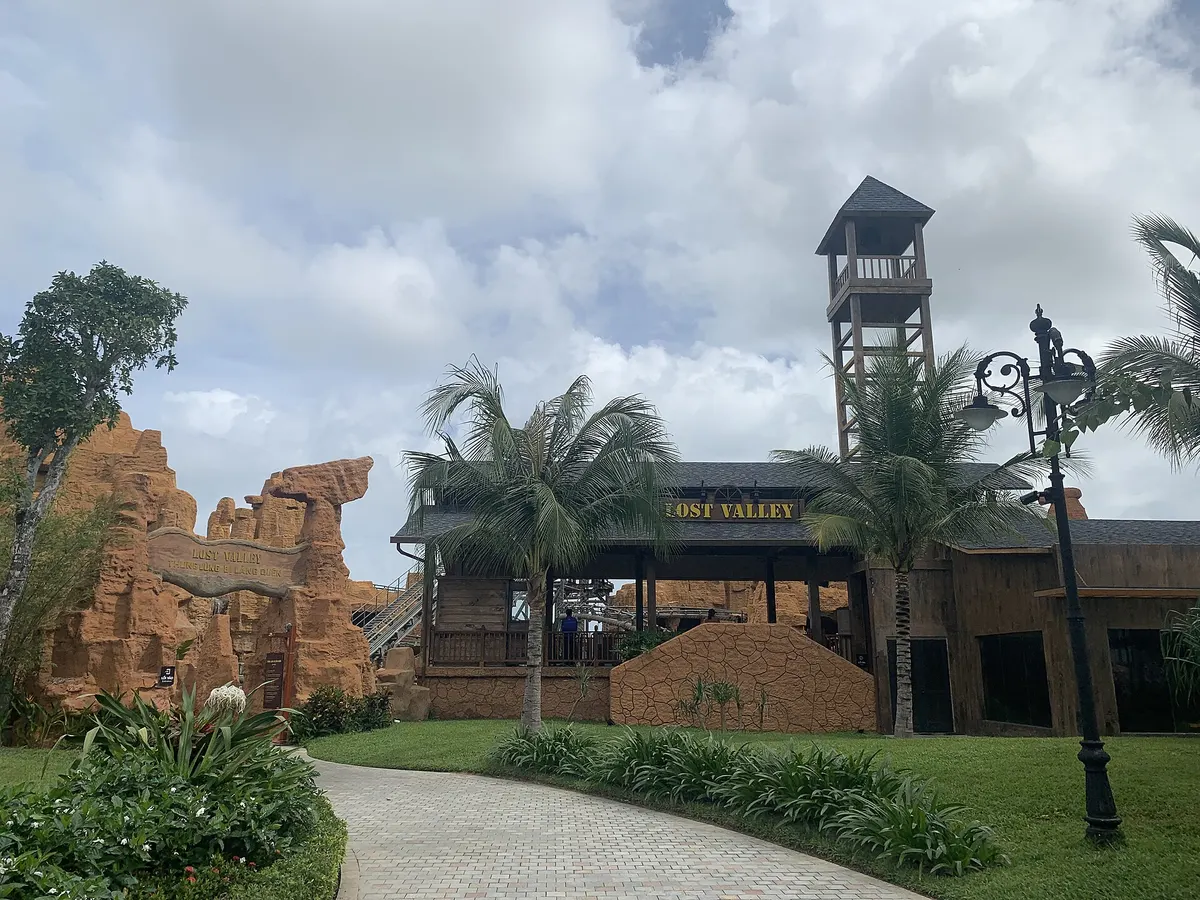 A wooden station building with a Lost Valley sign and a lookout tower, set among artificial orange rock formations and palm trees