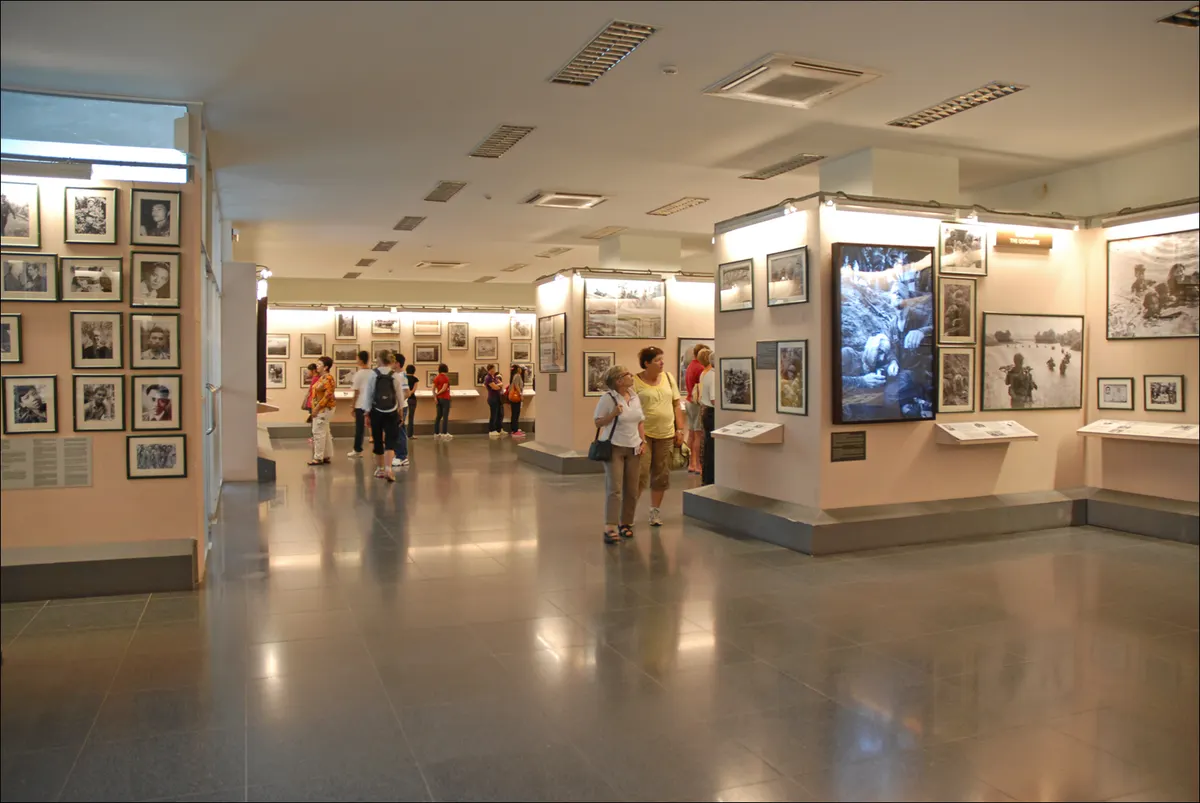 Visitors walking through a bright gallery hung with framed black-and-white war photographs