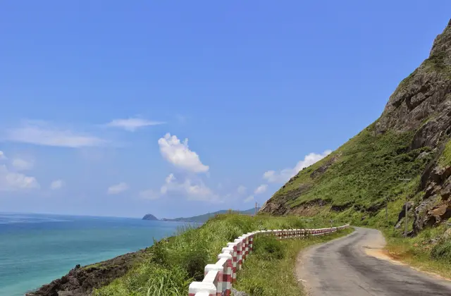 A coastal road curving above turquoise water under a blue sky on Con Dao