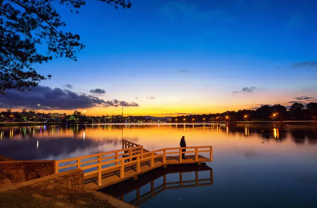 A person standing on a wooden pier over a lake glowing at sunset in Da Lat