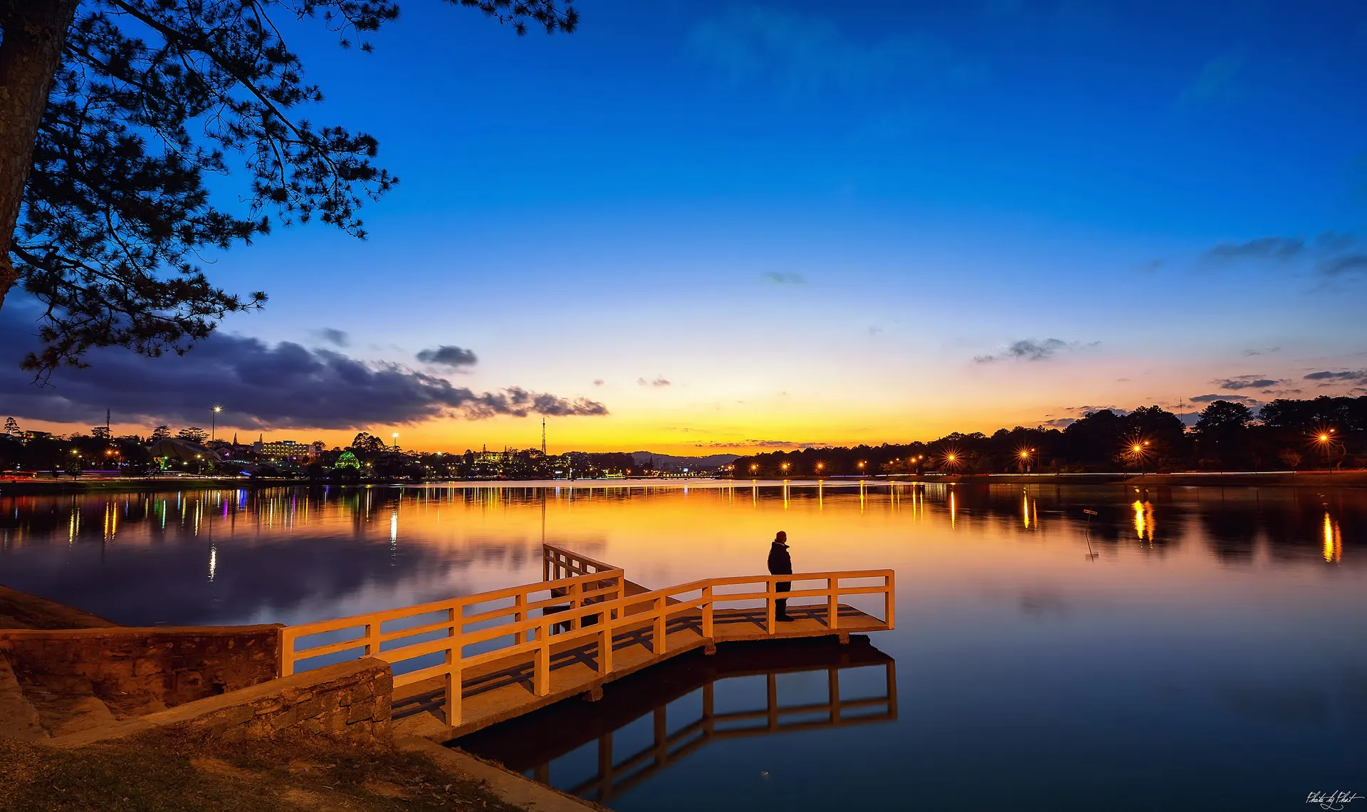 A person standing on a wooden pier over a lake glowing at sunset in Da Lat