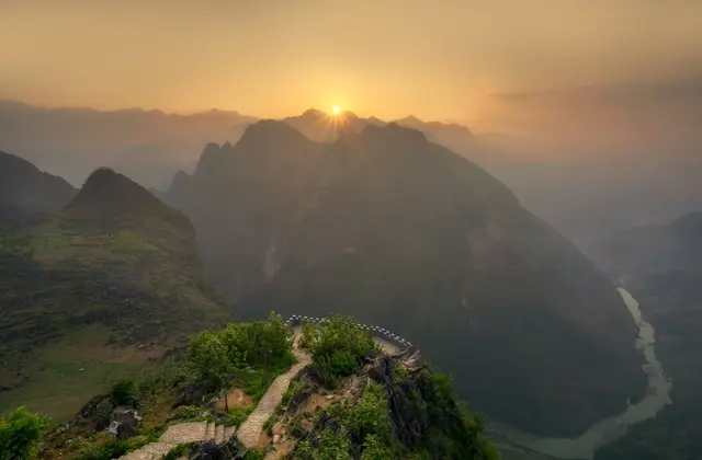 Sun rising through layered mountain ridges in Ha Giang, seen from a cliff-top path