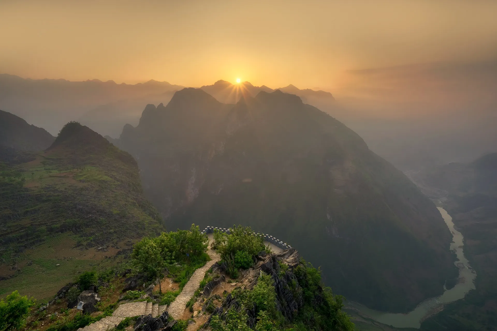 Sun rising through layered mountain ridges in Ha Giang, seen from a cliff-top path