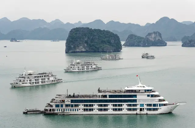 Cruise boats gliding between limestone islands in Ha Long Bay under a hazy sky