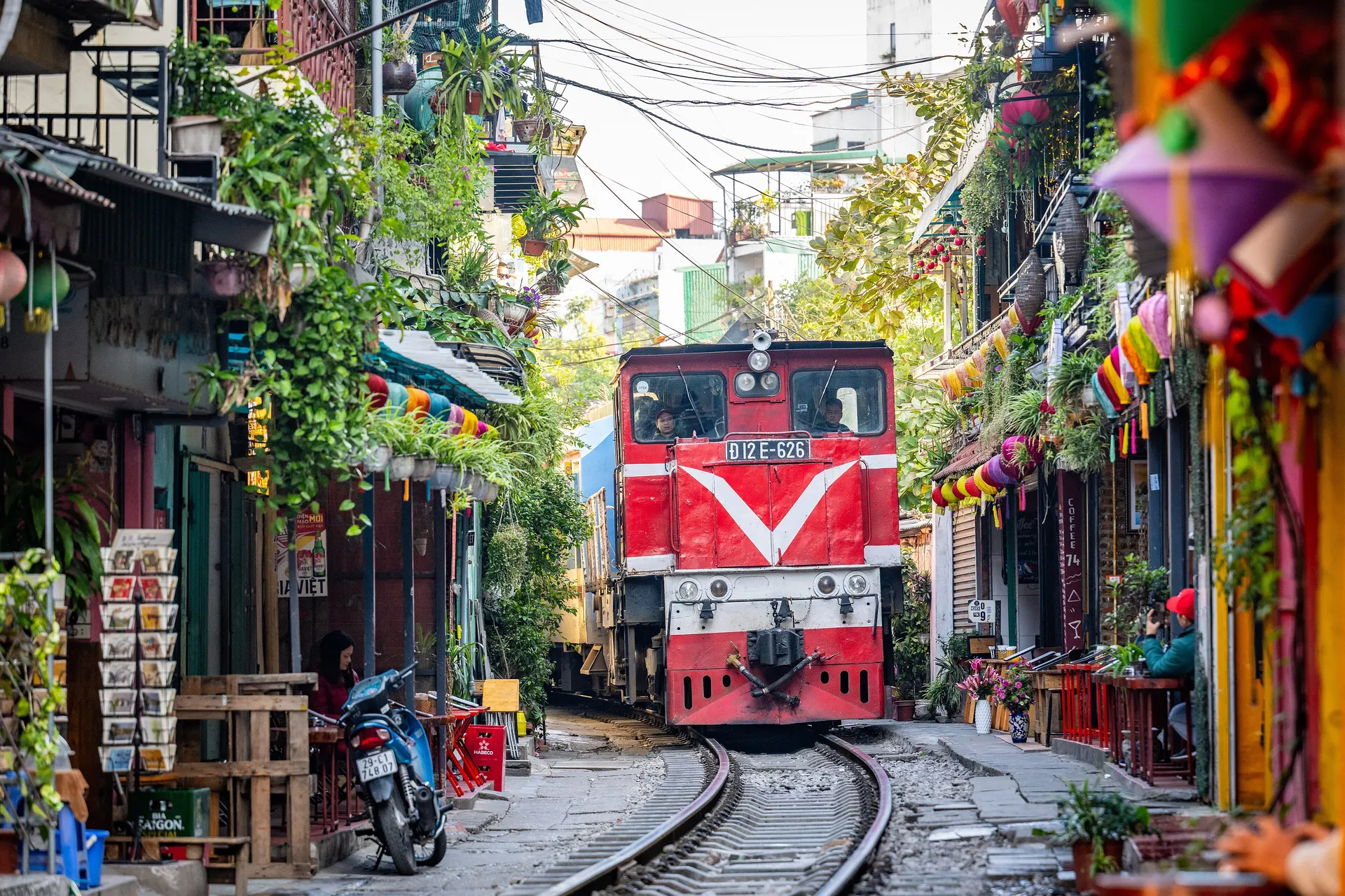 A red diesel train rolling down the narrow Hanoi Train Street between colorful houses
