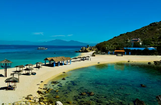 Turquoise water and thatched beach shelters on a curved sandy bay