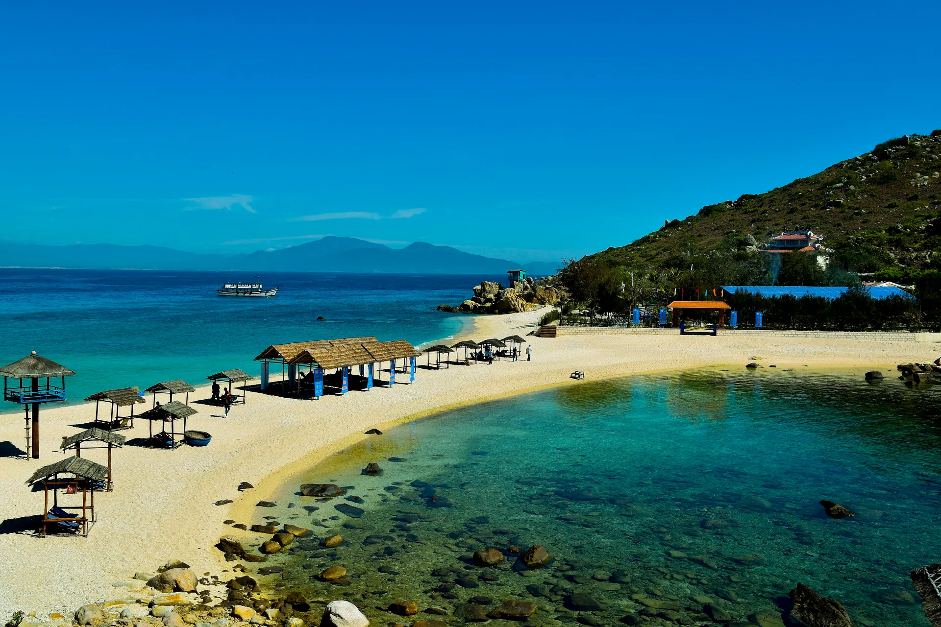 Turquoise water and thatched beach shelters on a curved sandy bay