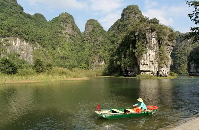 A rower guiding a small boat across a calm lake below limestone peaks in Ninh Binh