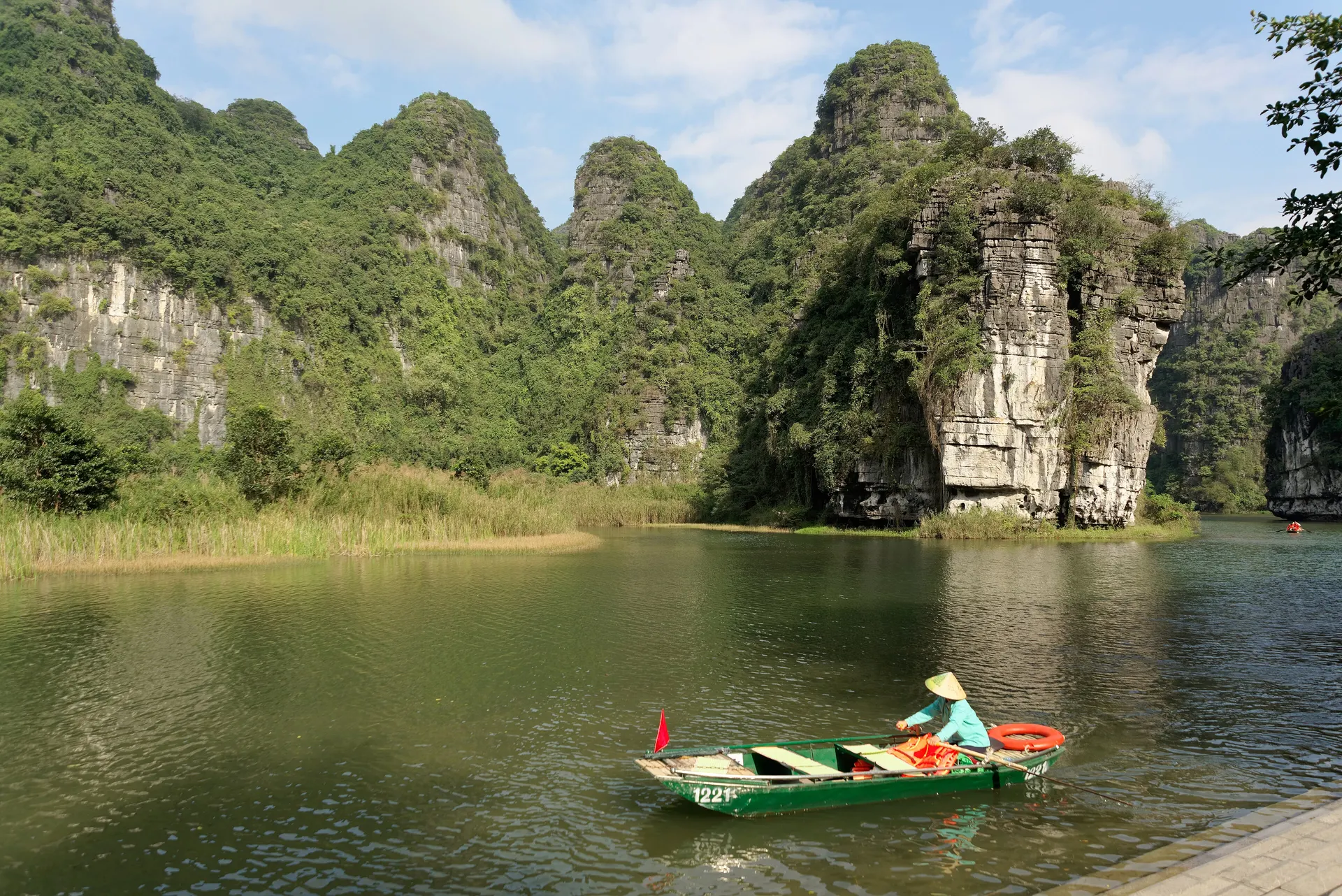 A rower guiding a small boat across a calm lake below limestone peaks in Ninh Binh