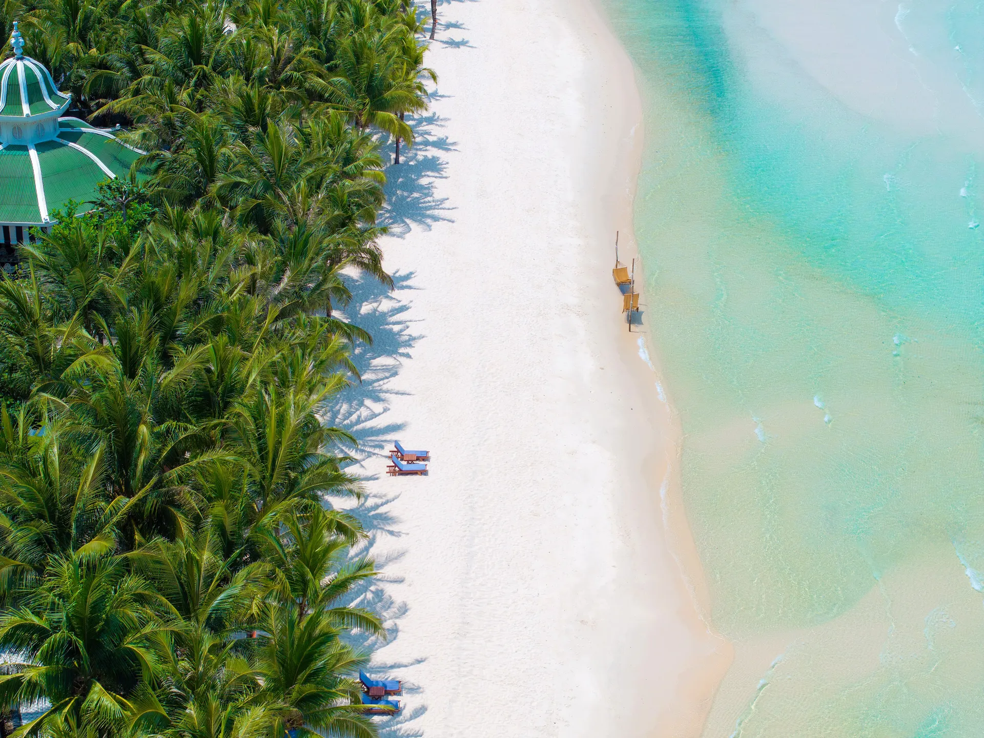 Aerial view of a white sand beach and turquoise shallows fringed by palms on Phu Quoc